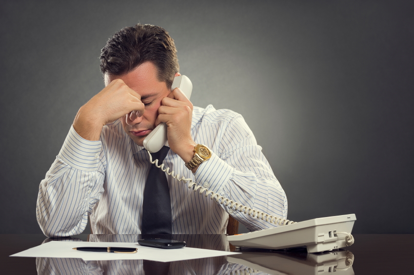 Easy On Hold | Blog - Overwhelmed businessman in white shirt and tie having a headache during a stressful phone conversation. Tired thoughtful businessman with one hand on his forehead taking a tedious phone call.