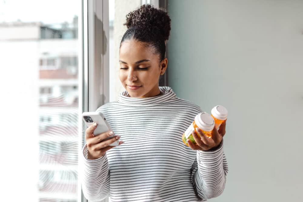 Young woman holding a smart phone and pill bottles